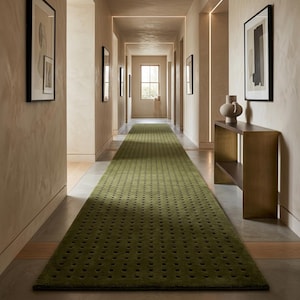May include: A long, rectangular runner rug in a deep olive green colour, featuring a repeating pattern of small, dark, square-shaped cutouts or indentations across its entire surface, laid out centrally along a hallway floor.