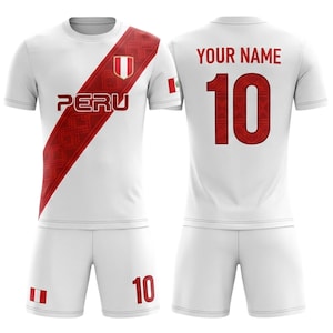 Peut inclure: Un uniforme de football blanc avec des détails rouges. Le maillot affiche le mot "PERU" et le numéro "10". Une bande diagonale rouge avec un motif géométrique et le drapeau péruvien est visible. Le short porte également le numéro "10".