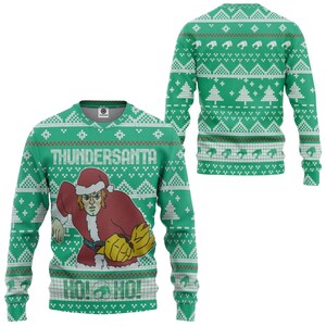 Puede incluir: Un suéter verde de manga larga con un patrón navideño blanco repetitivo de árboles y formas geométricas. El frente muestra un personaje con un traje de Santa rojo con el texto THUNDERSANTA arriba y HO! HO! con un logotipo debajo del personaje.