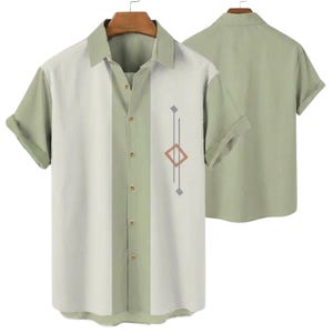 May include: A short-sleeved button-down shirt in sage green and off-white. The shirt features a vertical stripe design with a geometric pattern on the front. The shirt is displayed on a hanger, with a second shirt visible in the background.