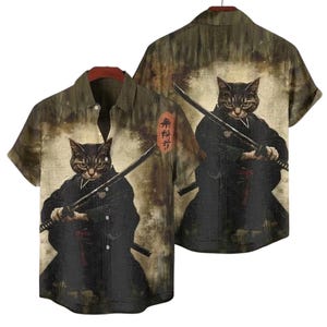 May include: Short-sleeved button-down shirt featuring a cat samurai design. The cat is depicted in a black kimono holding a katana. The shirt has a brown and beige background with Japanese text on the side.