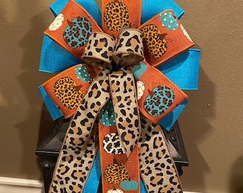 May include: A blue and orange bow with a leopard print ribbon and a pumpkin pattern. The bow is tied around a lantern.