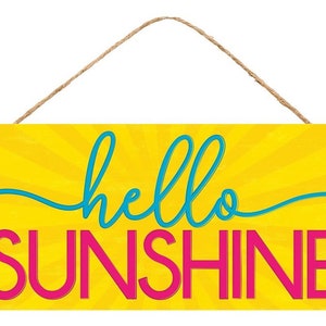 May include: A yellow wooden sign with a sunburst pattern and the text "hello sunshine" in blue and pink lettering. The sign has a twine hanger.