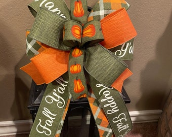 May include: A black lantern with a green, orange and white checked ribbon bow. The ribbon has the text "Happy Fall Y'all" and "Happy Fall" printed on it. The bow also has a green ribbon with a pumpkin print.