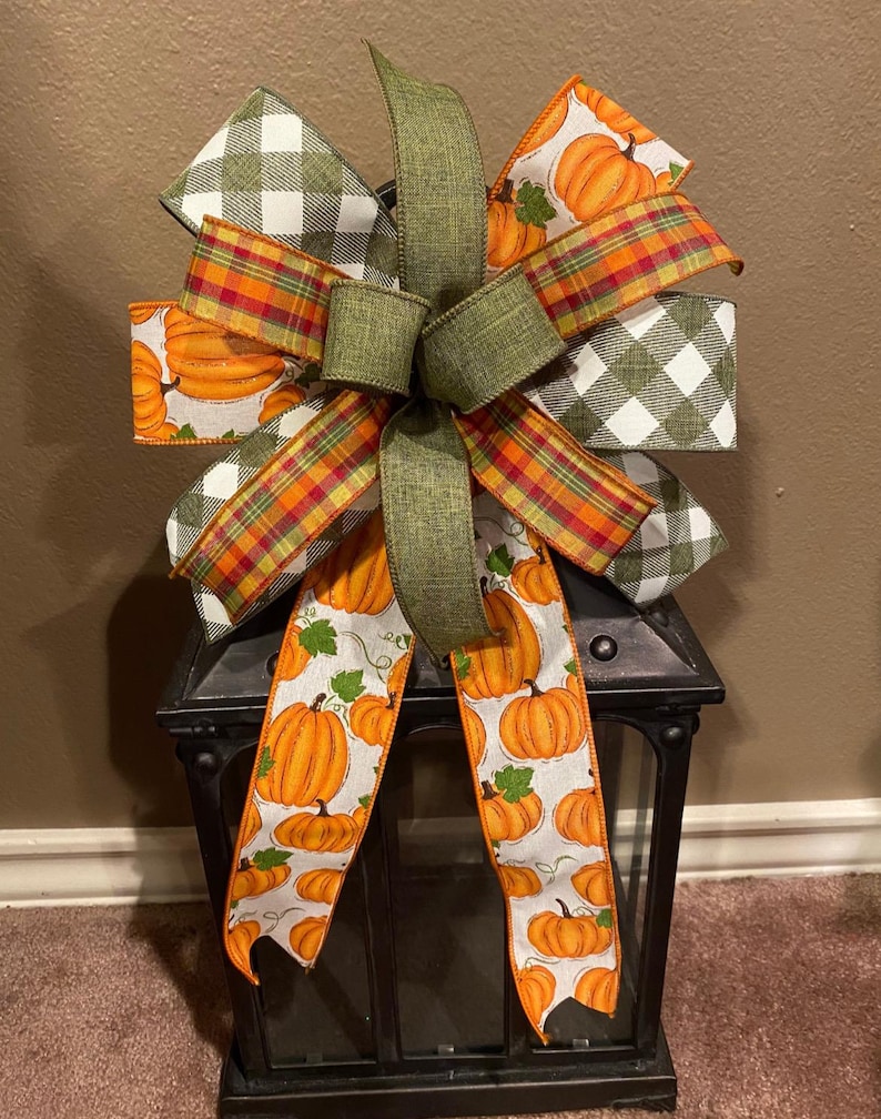 May include: A green, white, and orange plaid bow with a pumpkin print ribbon tied around a black metal lantern.