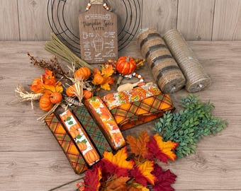 May include: A DIY wreath making kit featuring a black wire frame, a wooden sign labeled Homemade Pumpkin Spice Latte, two rolls of burlap mesh, assorted orange pumpkin picks, green foliage, and several spools of autumn-themed patterned ribbon.