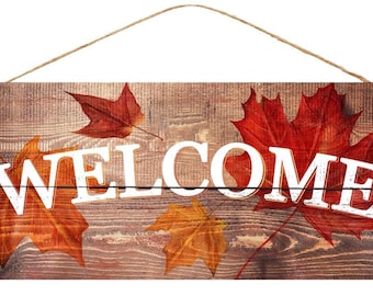 Puede incluir: Un letrero de madera con la palabra "WELCOME" en letras blancas sobre un fondo marrón. El letrero está decorado con hojas de otoño rojas, naranjas y amarillas.