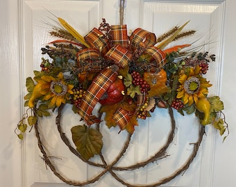 May include: A fall-themed wreath with a brown, woven base. The wreath is decorated with sunflowers, gourds, berries, and a plaid ribbon.