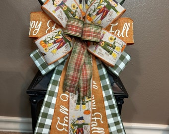 May include: A green and white buffalo check ribbon bow with a brown ribbon that says "Happy Fall Y'all" and a tan ribbon with a scarecrow design and the text "Fall"