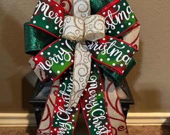 May include: A green, red, and white Christmas bow with the words "Merry Christmas" on it. The bow is tied around a black lantern.
