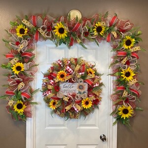 K&ouml;nnte beinhalten: Ein Sonnenblumenkranz mit einem rot-wei&szlig; karierten Band und einem Schild mit der Aufschrift "hello sunshine". Zwei passende Sonnenblumen-Girlanden mit rot-wei&szlig; kariertem Band befinden sich auf beiden Seiten des Kranzes.
