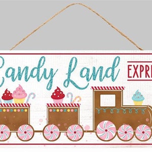 May include: A white wooden sign with a gingerbread train and the words "Candy Land Express" in blue glitter lettering. The train has three cars with candy cane wheels and is decorated with cupcakes.