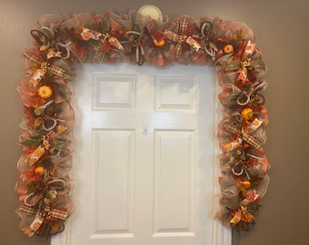 May include: A fall-themed door swag with orange, brown, and green mesh, accented with faux pumpkins, leaves, and berries.
