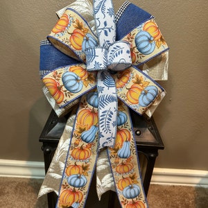 May include: A blue, white, and brown ribbon bow with a pumpkin pattern. The bow is tied around a black lantern.