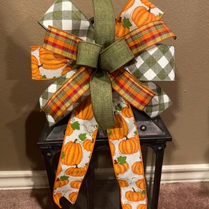 May include: A green, red, and white plaid bow with a pumpkin print ribbon tied around a black lantern.