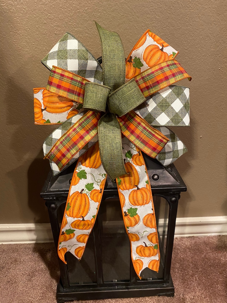 May include: A green, red, and white plaid bow with a pumpkin print ribbon tied around a black lantern.