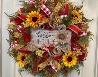 May include: A sunflower wreath with red and yellow ribbon, burlap, and a sign that says "hello sunshine".