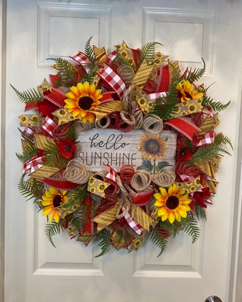 K&ouml;nnte beinhalten: Ein Sonnenblumenkranz mit rotem und gelbem Band, Sackleinen und einem Schild mit der Aufschrift "Hallo Sonnenschein".