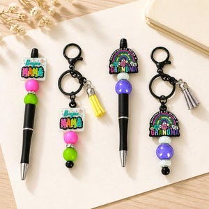 May include: Four black pens and keychains with decorative beaded accents. Two pens have "Boujee Mama" text, and two have "Happiness is being a Grandma" text. The pens and keychains have a variety of colorful beads and tassels.