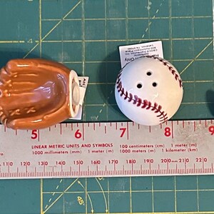 Puede incluir: Un juego de salero y pimentero con tem&aacute;tica de b&eacute;isbol. El juego incluye una gorra de b&eacute;isbol roja y azul marino, un guante de b&eacute;isbol marr&oacute;n, una pelota de b&eacute;isbol blanca con costuras rojas y un bate de b&eacute;isbol de madera.