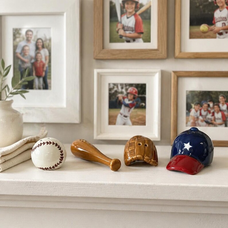Puede incluir: Un juego decorativo con tem&aacute;tica de b&eacute;isbol que presenta una pelota de b&eacute;isbol blanca con costuras marrones, un bate de madera, un guante marr&oacute;n y una gorra de b&eacute;isbol azul y roja. Fotos familiares en marcos blancos y de madera en el fondo.
