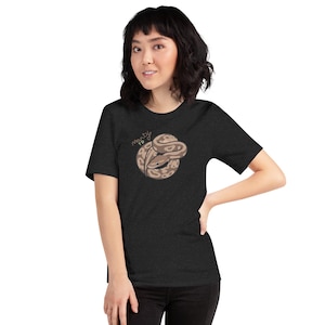 May include: A dark charcoal grey short-sleeve t-shirt featuring a graphic illustration of a coiled brown and tan snake. The text "Monty TD" is written in a light-coloured, cursive script above the snake illustration on the front of the shirt.