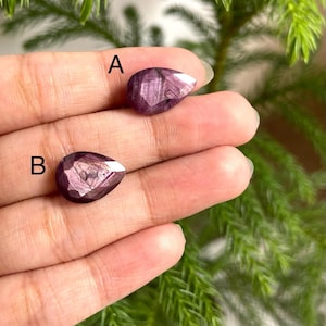 Peut inclure: Deux pierres précieuses taillées en forme de poire, dans des tons violets et roses, sont présentées. Les pierres précieuses sont tenues dans une main, avec un fond de feuillage vert. Les pierres précieuses sont étiquetées A et B.