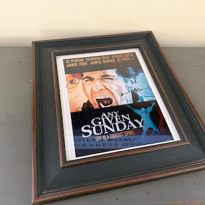 May include: Framed movie poster for "Any Given Sunday" with Al Pacino. The poster features a close-up of a man yelling, with the film's title and tagline. The frame is black with a brown inner edge.