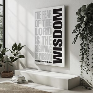 May include: A rectangular canvas print with the text "THE FEAR OF THE LORD IS THE BEGINNING OF WISDOM" in gray and black. The word "WISDOM" is vertically aligned on the right side. The print is displayed in a minimalist interior setting.