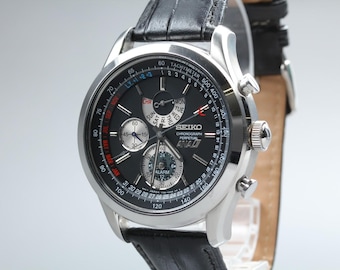May include: A Seiko Chronograph Perpetual ANA-DI wristwatch with a black dial, silver-tone hands, and multiple sub-dials. The watch features a tachymeter scale on the outer rim, a date display, and a black leather strap with a silver buckle.