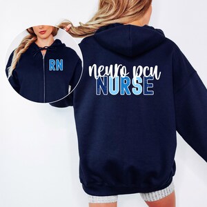 May include: Navy blue zip-up hoodie with the text "neuro pcu NURSE" in white and blue lettering on the back. The front features the letters "RN" in blue. The hoodie has a drawstring hood.