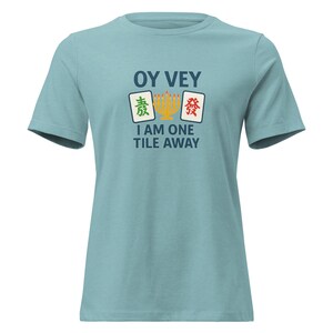 May include: Light blue t-shirt with the text "OY VEY" above a graphic of Mahjong tiles and the phrase "I AM ONE TILE AWAY". The graphic includes green, yellow, and red accents. The shirt is a short-sleeved crew neck.