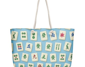 May include: A large tote bag with a light blue background and a repeating pattern of Mahjong tiles. The tiles are white with various symbols and characters in green, red, and black. The bag has white rope handles.