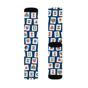 Op de afbeelding: Een paar sokken met een diepblauwe achtergrond en een herhalend patroon van witte mahjongtegels. De tegels tonen diverse symbolen, waaronder rode Chinese karakters, groen bamboe, kleurrijke bloemen, een menora en een blauwe Davidster.