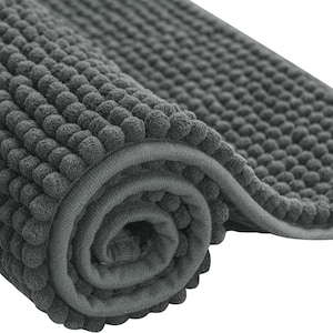 May include: A rolled-up, dark gray bath mat with a textured, bubble-like surface. The mat has a soft, plush appearance and a bound edge. The close-up shot highlights the detailed texture and the rolled portion of the mat.