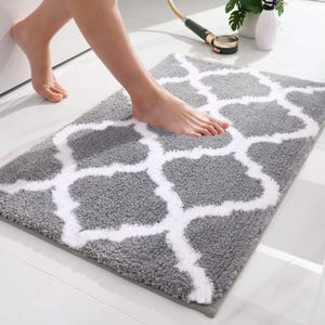May include: A rectangular gray bath mat with a white geometric pattern. The mat is made of a soft, plush material. The mat is approximately 24 inches long and 16 inches wide.