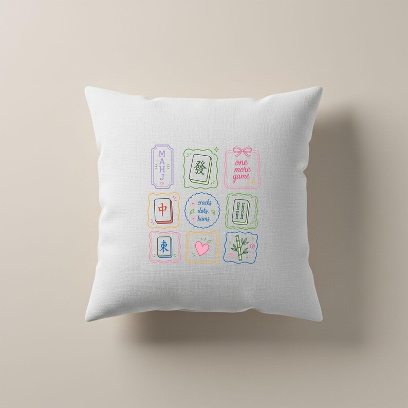 May include: A white square throw pillow featuring a central grid of nine colorful illustrations related to Mahjong. The designs include Mahjong tiles, a pink heart, bamboo stalks, and text that reads MAHJ, one more game, and cracks dots bams.