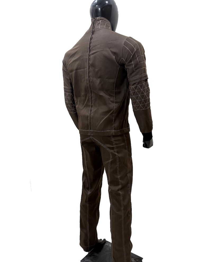 Może przedstawiać: Brązowy dwuczęściowy garnitur prezentowany na manekinie. Kurtka ma geometryczne przeszycia na ramionach i rękawach. Spodnie mają białe przeszycia wzdłuż szw&oacute;w. Manekin ma czarną głowę i czarne rękawiczki.