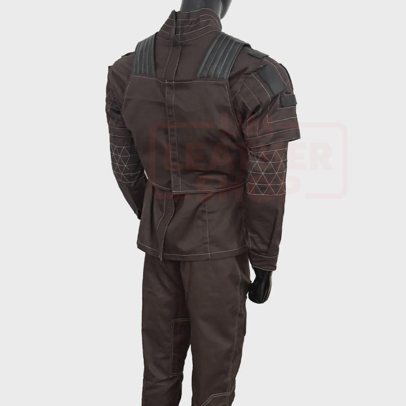 May include: Brown tactical jacket and pants set. The jacket features a high collar, shoulder padding, and geometric stitching on the sleeves. White stitching outlines the seams. The pants have a matching color and style. The outfit is displayed on a mannequin.