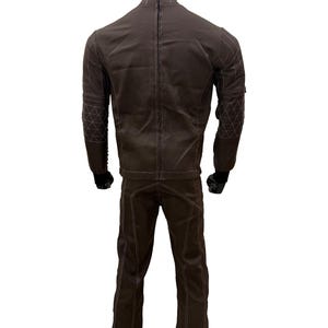 Może przedstawiać: Brązowy zestaw kurtka i spodnie. Kurtka ma wysoki kołnierz i białe przeszycia. Spodnie mają proste nogawki z pasującymi przeszyciami. Rękawy kurtki mają geometryczny wz&oacute;r na ramieniu.