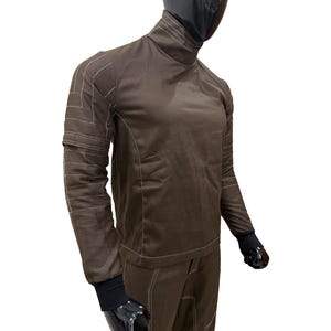 Może przedstawiać: Brązowy kombinezon z białymi detalami szw&oacute;w. Str&oacute;j posiada wysoki kołnierz, długie rękawy i pasujące spodnie. Rękawy mają czarne mankiety. Głowa manekina jest czarna.