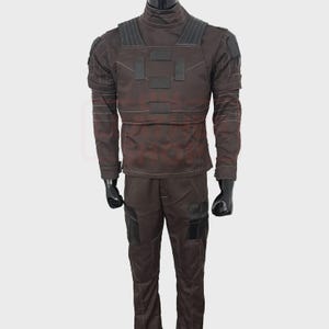 May include: A brown tactical uniform set, including a long-sleeved jacket and pants. The jacket features a high collar, reinforced shoulders, and multiple pockets. The pants have pockets and reinforced knee areas. The uniform is designed for durability and functionality.