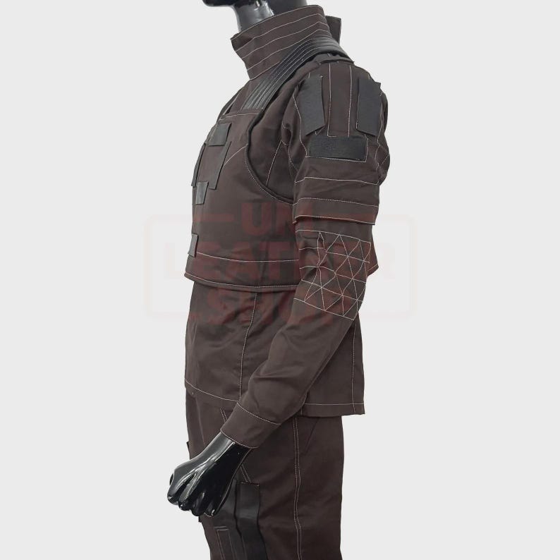 May include: A brown tactical outfit with a high collar and multiple panels. The outfit features white stitching and geometric patterns on the sleeves. The mannequin is wearing a black head covering and gloves.