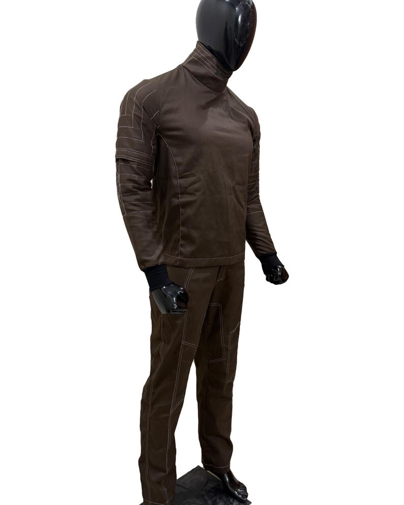 Może przedstawiać: Brązowy dwuczęściowy str&oacute;j z białymi przeszyciami. G&oacute;ra to golf z długim rękawem, a spodnie mają proste nogawki. Manekin ma na sobie czarne rękawiczki i buty.