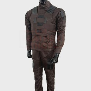May include: A brown tactical uniform displayed on a mannequin. The outfit includes a long-sleeved shirt with a high collar, a chest rig with black patches, and matching pants. White stitching details the seams and accents the design.