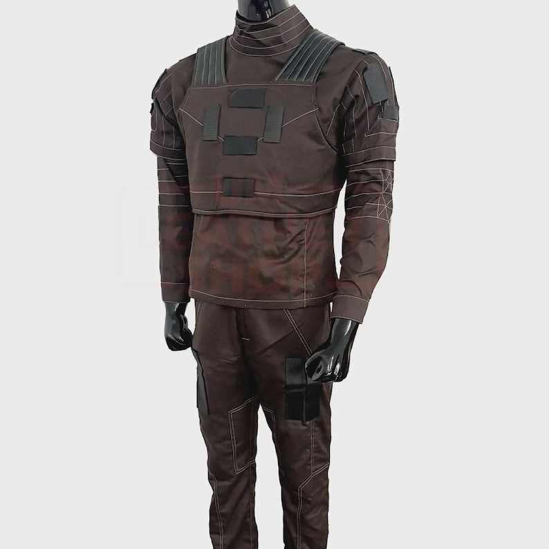 May include: A brown tactical uniform displayed on a mannequin. The outfit includes a long-sleeved shirt with a high collar, a chest rig with black patches, and matching pants. White stitching details the seams and accents the design.