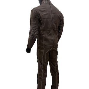 Może przedstawiać: Brązowy dwuczęściowy garnitur prezentowany na manekinie. Kurtka ma geometryczne przeszycia na rękawach i ramionach. Spodnie mają pasujące przeszycia. Garnitur jest wykonany z wytrzymałego materiału.