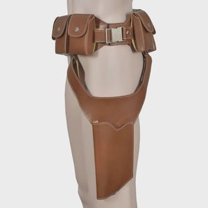 K&ouml;nnte beinhalten: Brauner Leder-Utility-G&uuml;rtel mit mehreren Taschen und einem Holster. Der G&uuml;rtel hat eine silberfarbene Schnalle und ist f&uuml;r das Tragen um Taille und Oberschenkel konzipiert. Die Taschen haben Knopfverschl&uuml;sse und wei&szlig;e N&auml;hte.