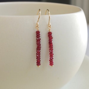 May include: A pair of gold dangle earrings with a long line of red gemstone beads.