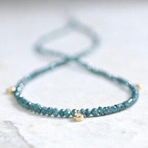 May include: A delicate necklace made with blue green gemstones and a single diamond accent. The necklace is made with small, round beads and has a simple, elegant design.